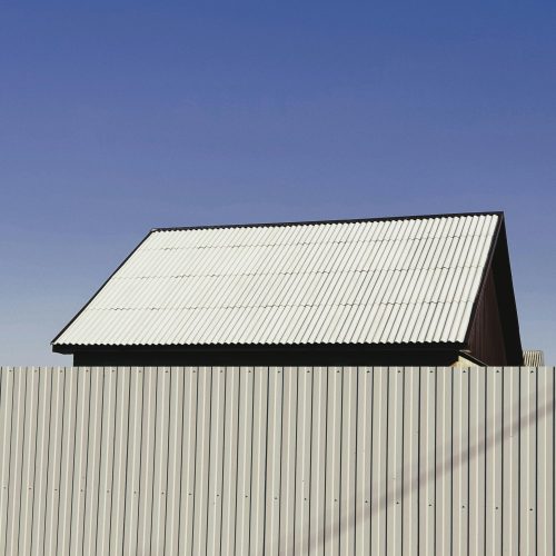 A simple structure with a metal roof and fence under a clear blue sky, showcasing minimalist architecture.